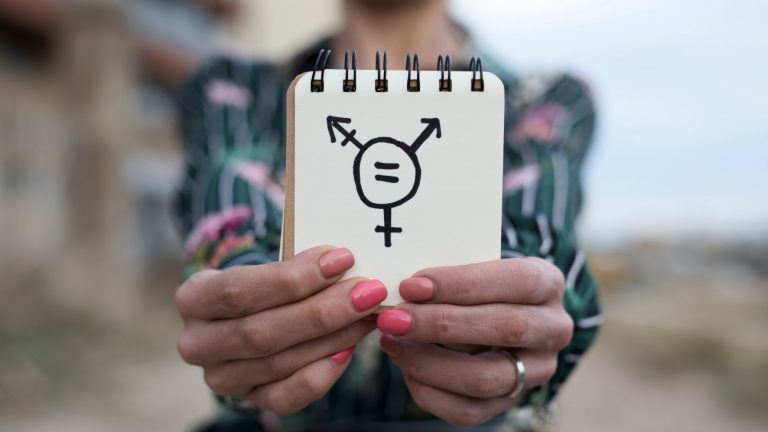 Une femme trans tenant une carnet sur lequel le symbole transgenre est tracé au feutre