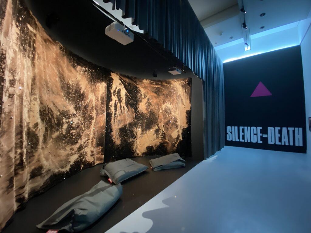 Vue d'une salle de l'exposition « Aux temps du sida » avec les rideaux de Jean-Luc Verna et le logo SILENCE = MORT conçu par Avram Finkelstein